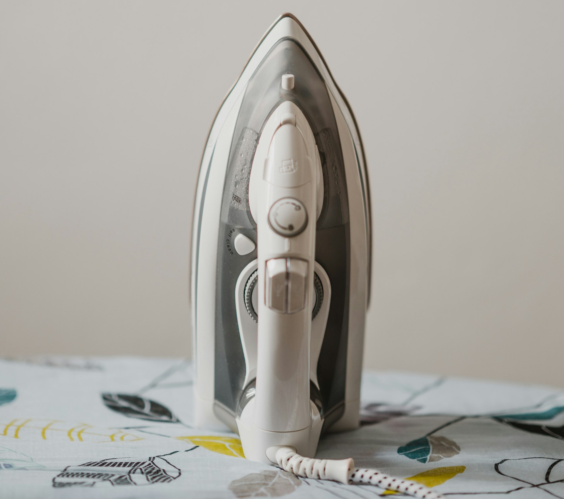 A white steam pressing iron standing on an ironing board